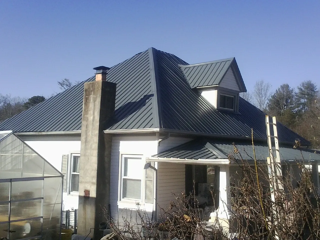 Dark blue standing seam metal roof on a white farmhouse with dormer — Slate & Tile Roof Repair by Roofing Brothers in Loveville