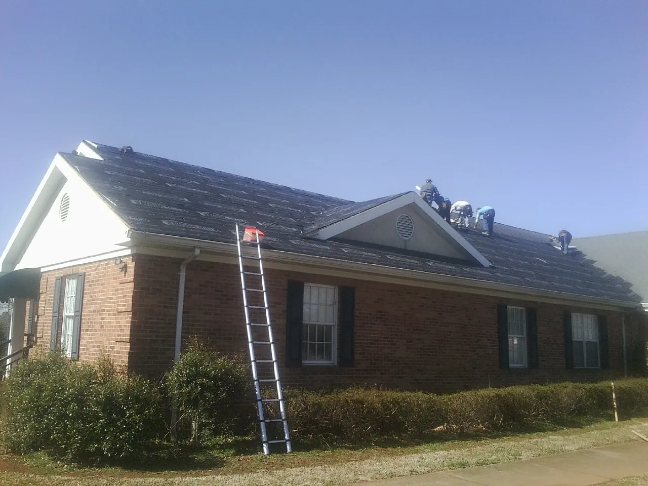 Crew tearing shingles off a brick ranch roof with a ladder set — Metal Roof Repair work by our crew in Loveville