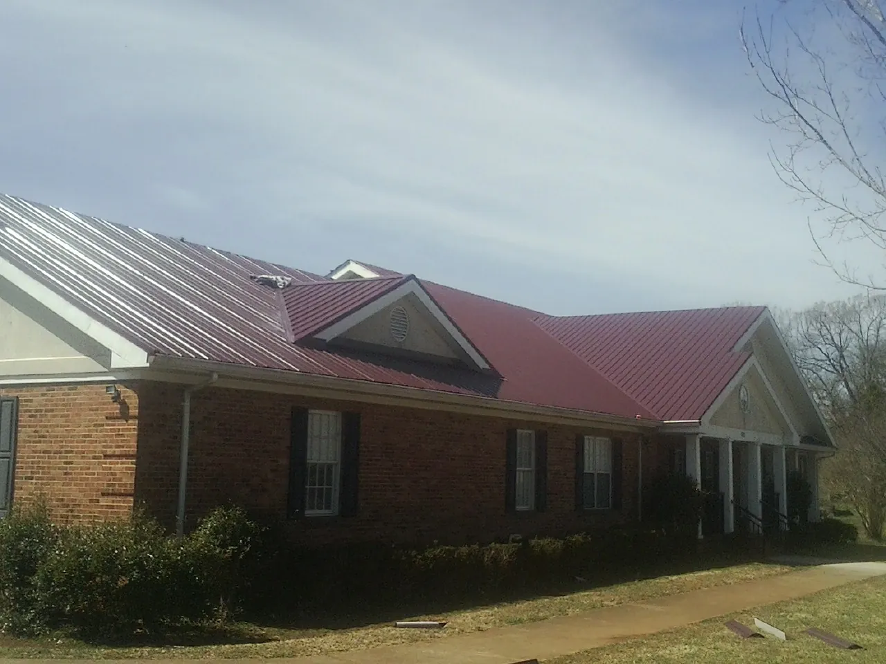Red metal roof with gabled entries on a long brick building, from a Hail Damage Roof Repair job in Loveville