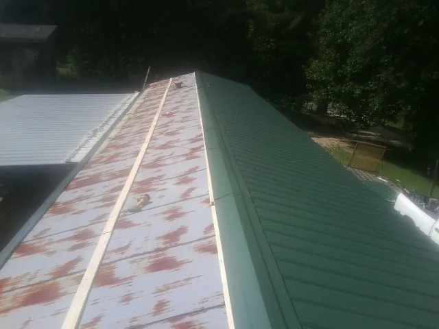 Old rusted panels beside newly installed green metal roofing — Wind Damage Roof Repair by Roofing Brothers in Loveville