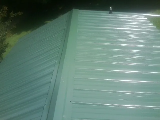 New green metal panels meeting at the ridge of a roof — Flat Roof Repair work by our crew in Loveville