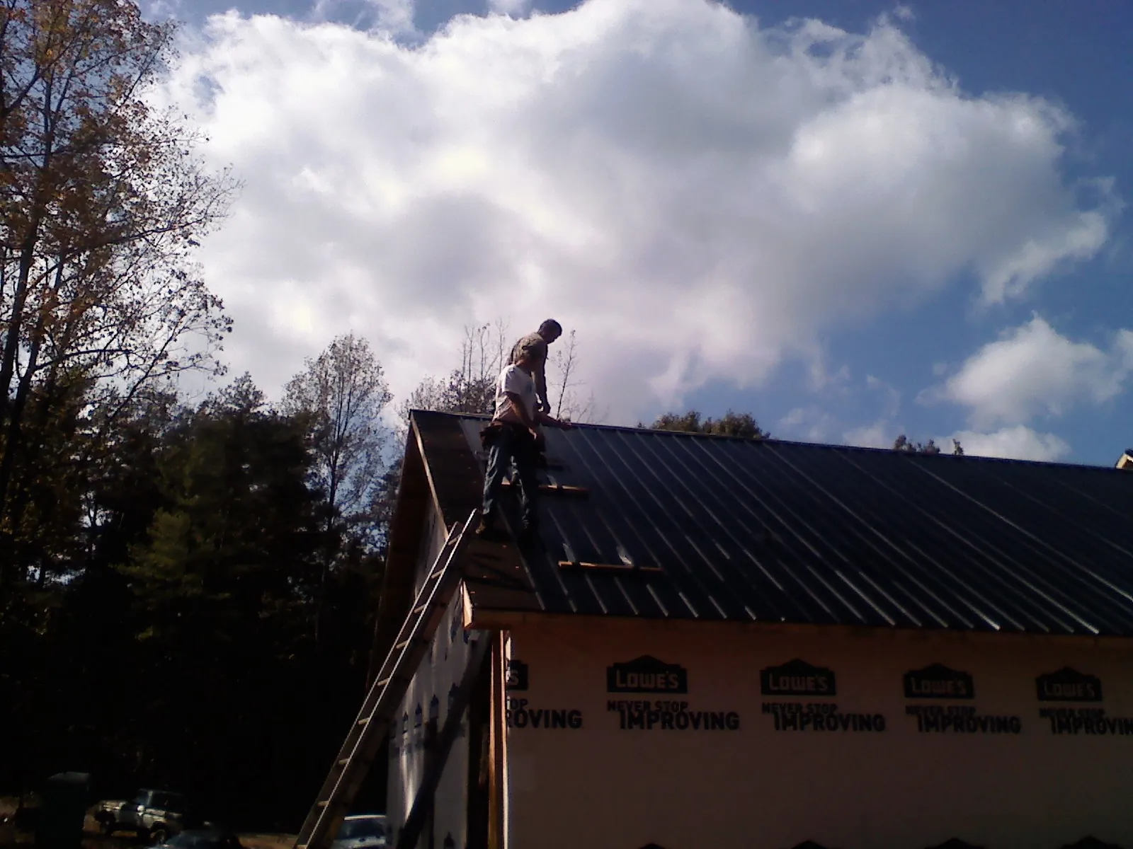 Roofer fastening dark metal panels high against a cloudy sky, from a Roof Inspection job in Loveville