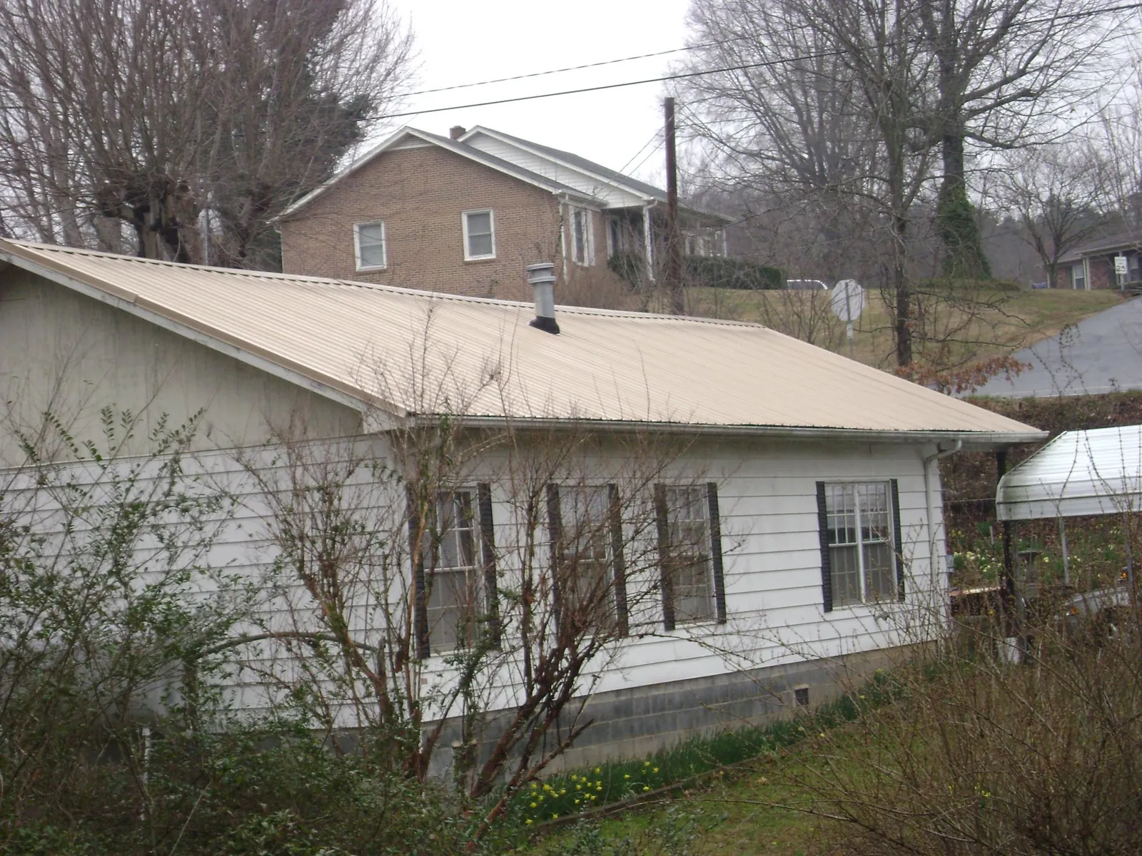 Tan metal roof on a white sided house set into a hillside — Commercial Roofing by Roofing Brothers in Loveville