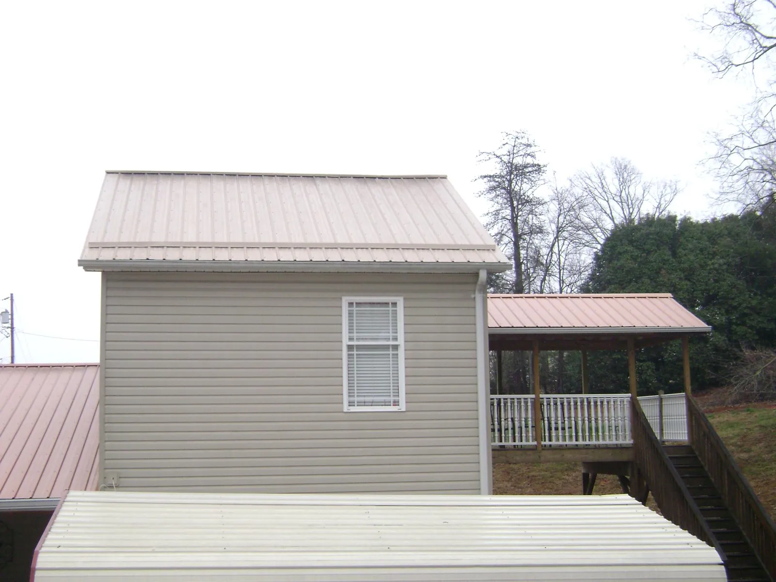 Tan metal roofs on a two story addition and attached porch, from a Roof Replacement job in Loveville